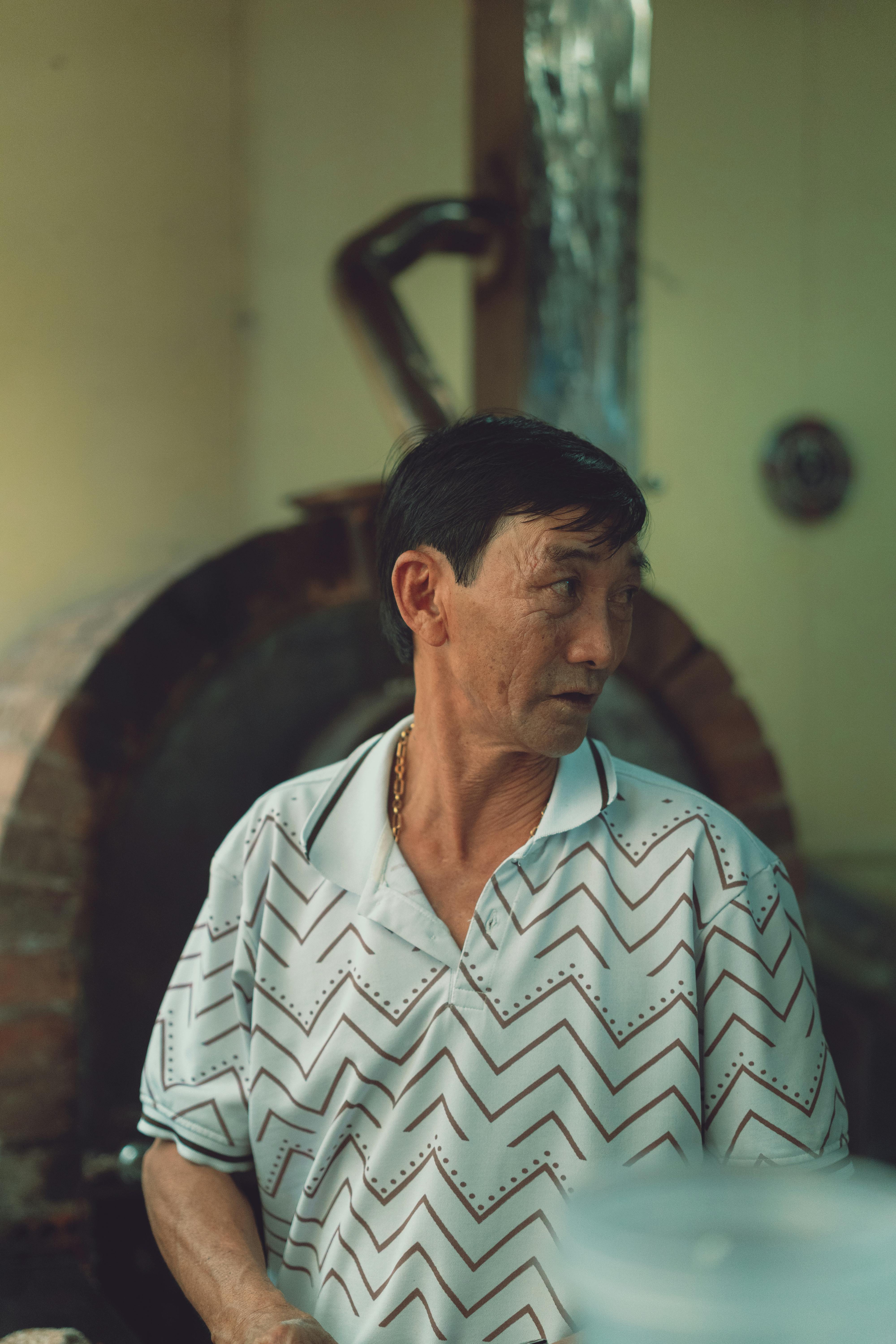 a man in a white shirt and blue jeans standing in front of a brick oven