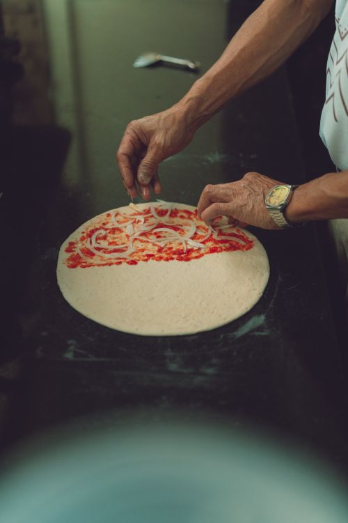 Free A man skillfully spreads tomato sauce on fresh pizza dough, showcasing culinary art. Stock Photo
