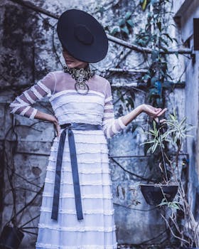 一位穿着复古连衣裙、戴着帽子的时尚女性在户外举着一株悬挂的植物摆姿势