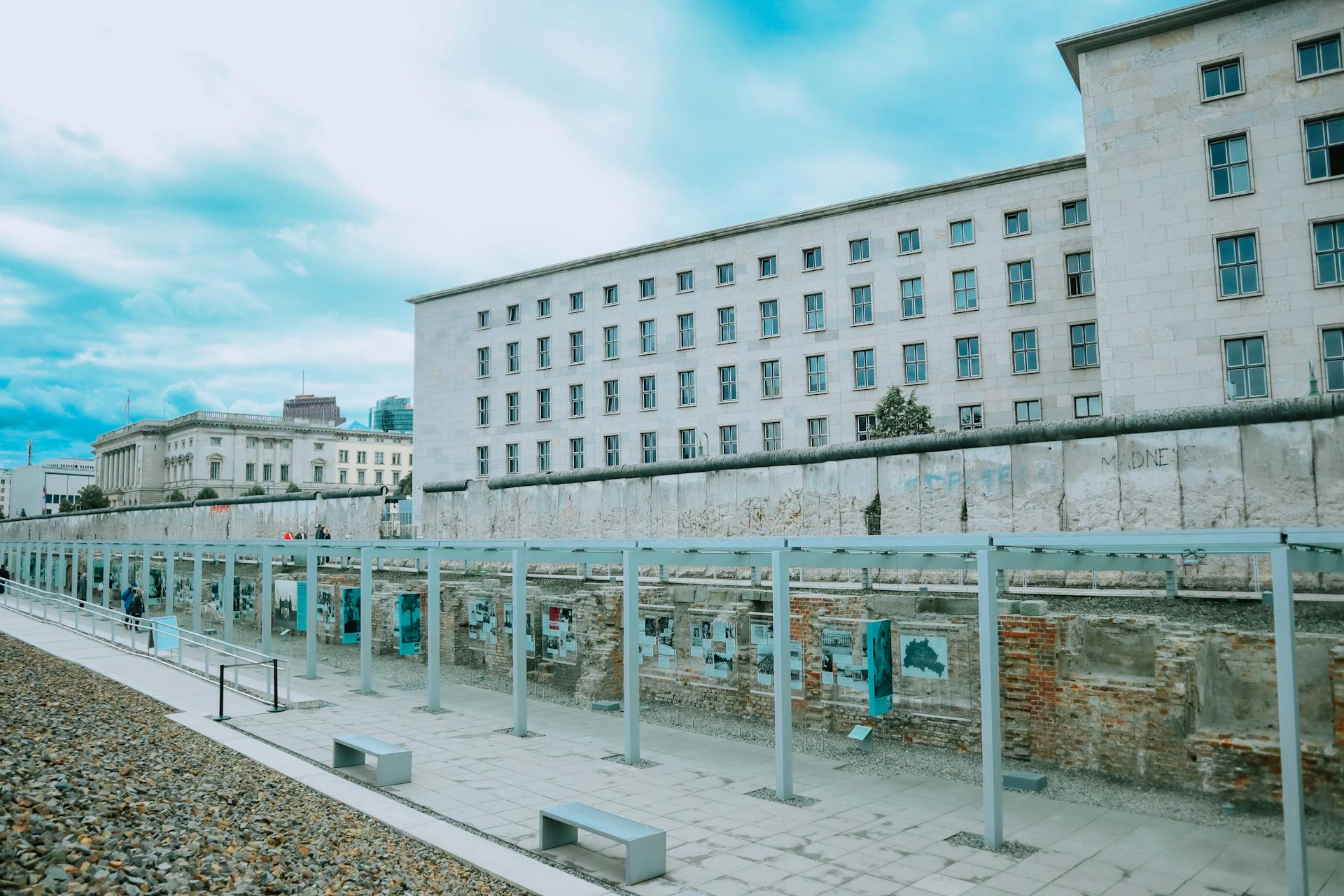 A view of the Berlin Wall remains with modern city backdrop on a cloudy day.