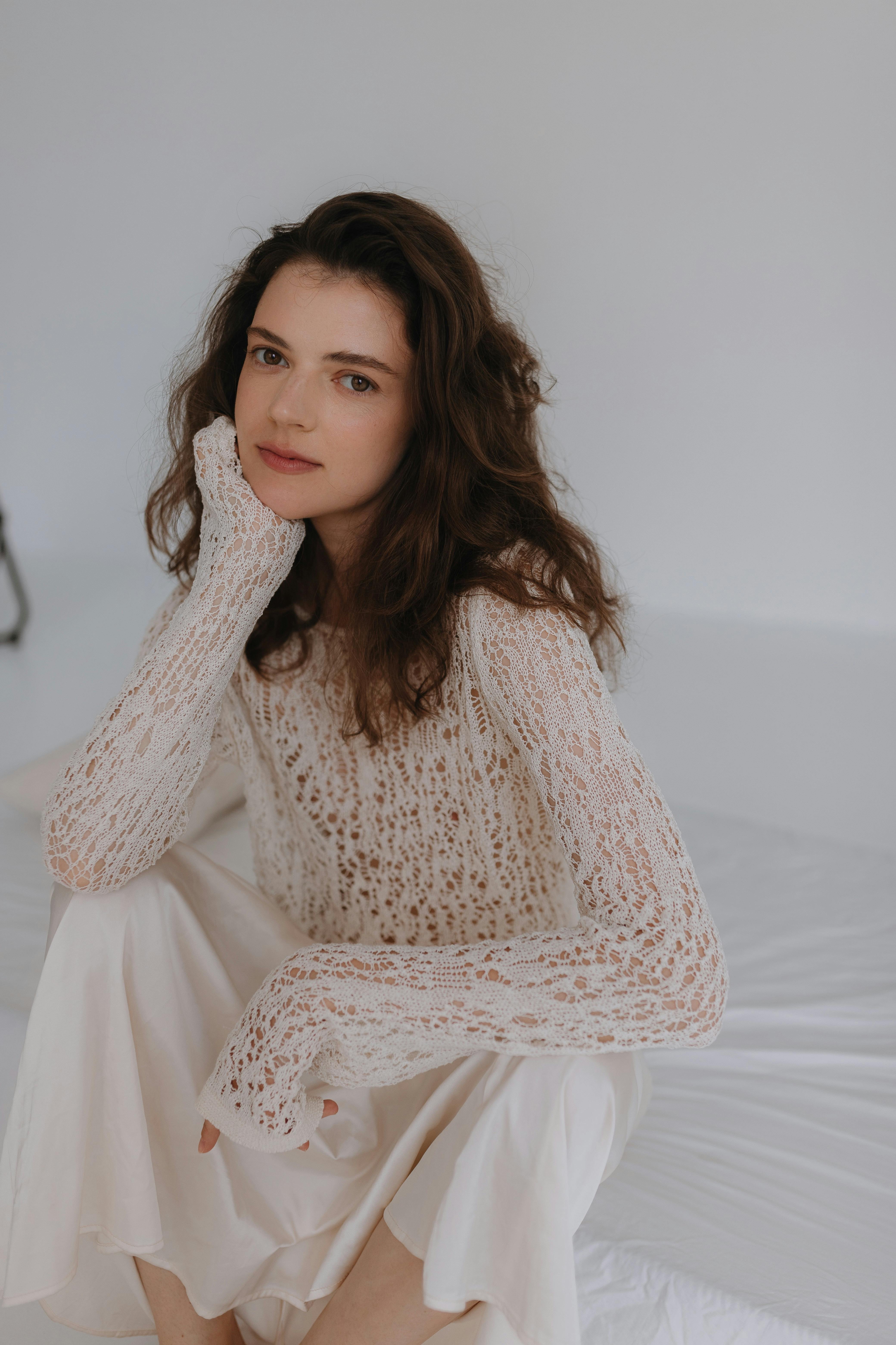 a woman in a white sweater and skirt sitting on a bed