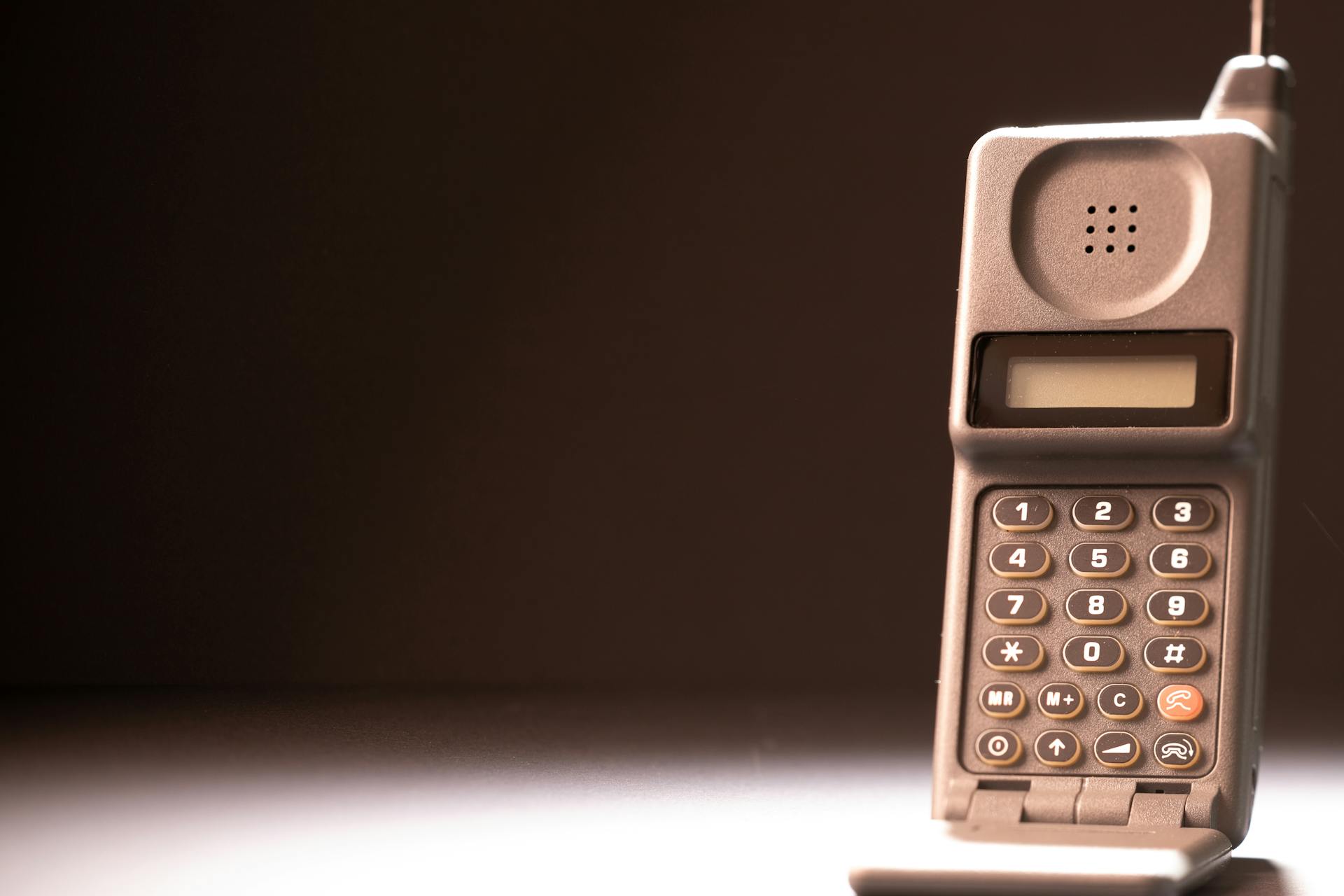 Vintage mobile phone with keypad and antenna on a dark background, emphasizing retro technology.