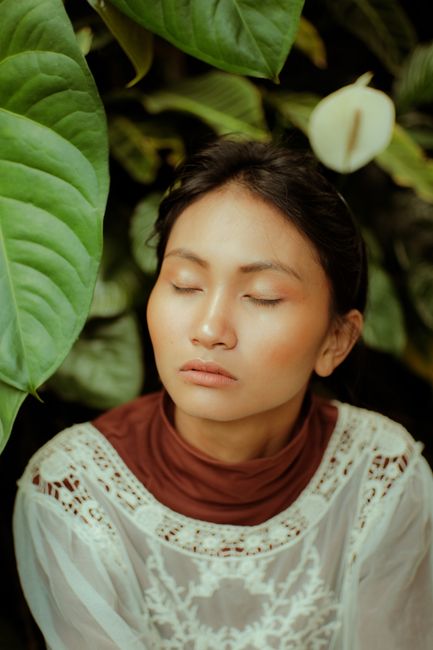 A serene portrait of a woman surrounded by vibrant green leaves in a natural setting.
