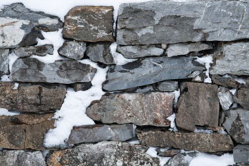 Free Close-up of a rugged stone wall with patches of snow, highlighting winter textures. Stock Photo