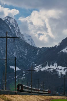 Train traveling through picturesque snowy mountains under dramatic sky, perfect for travel and nature themes.