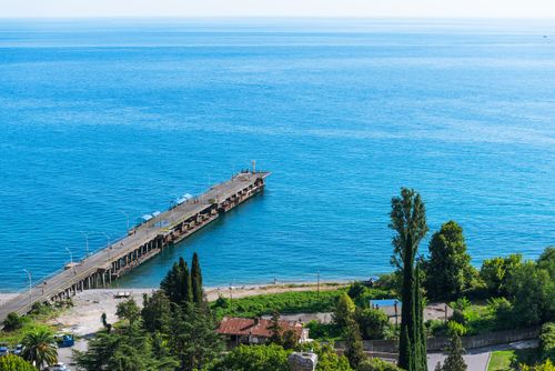 Free A captivating aerial view of a coastal pier extending into a vibrant blue ocean beneath a clear sky. Stock Photo