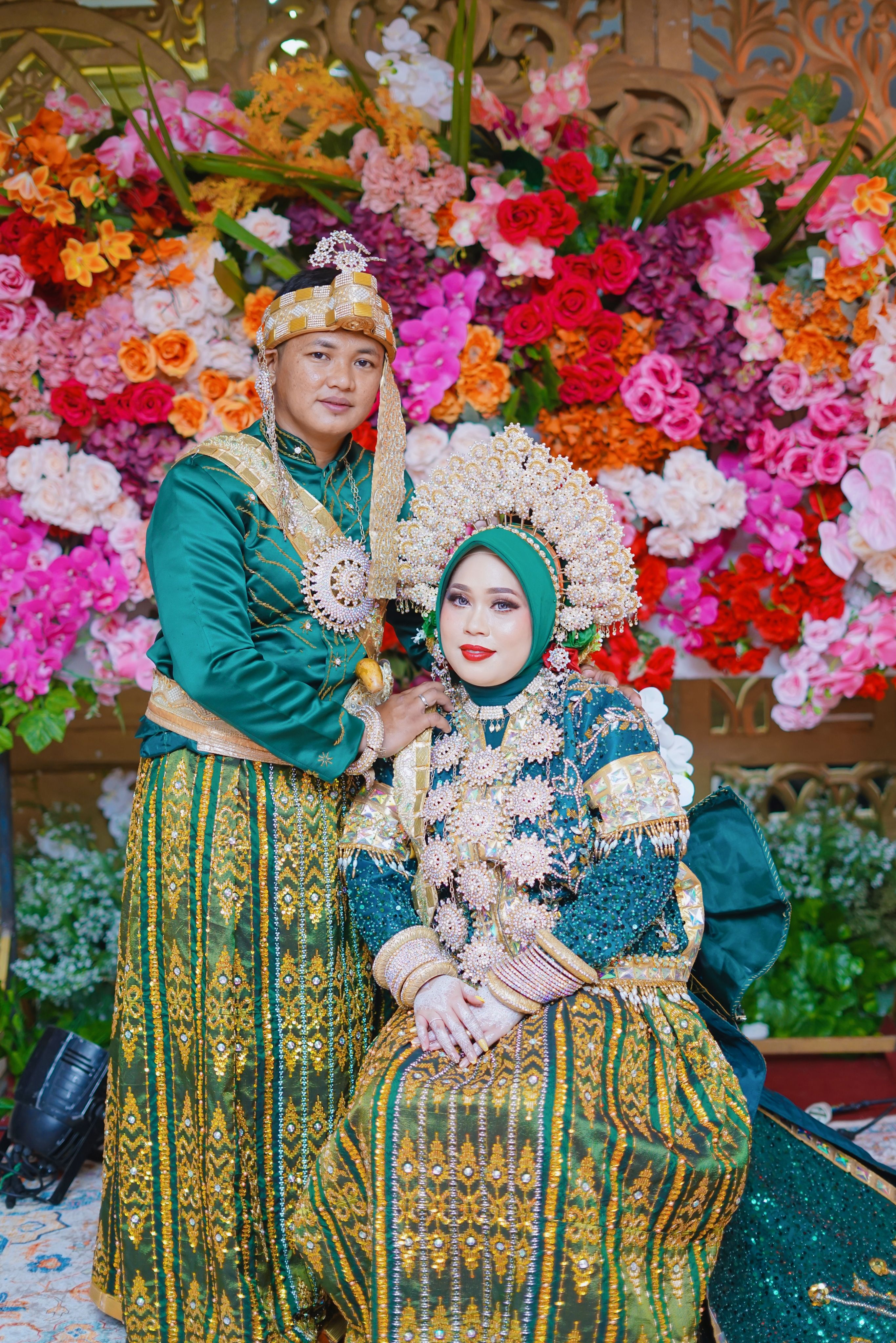 Vibrant Makassar wedding attire with colorful floral backdrop in Indonesia.