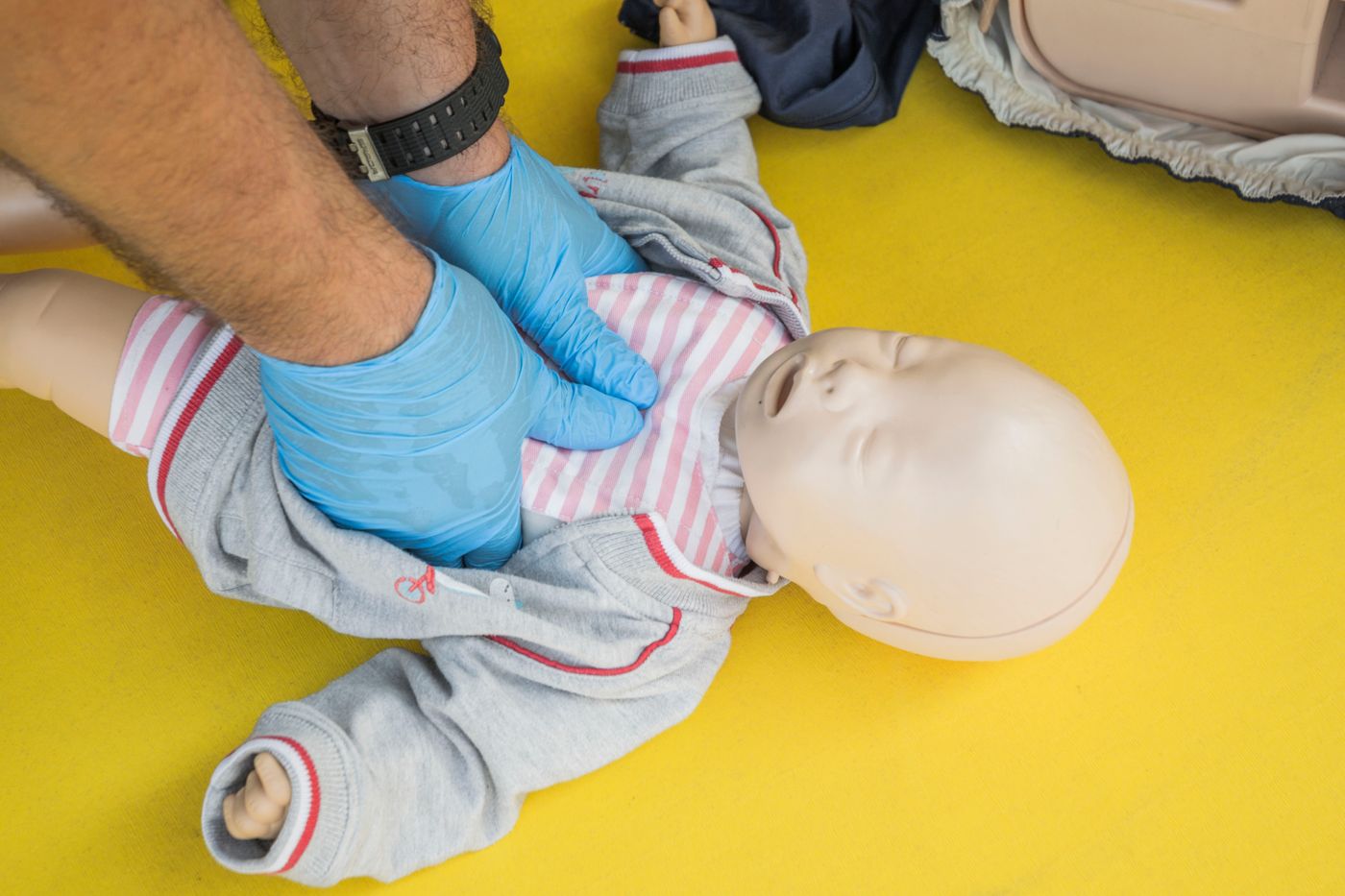 Infant first aid training using a baby manikin on a yellow mat (illustrative stock photo)