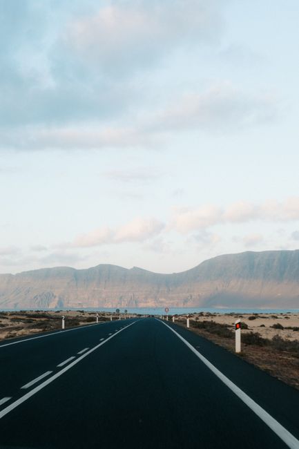 A long, straight highway leading towards distant mountains under a clear sky.