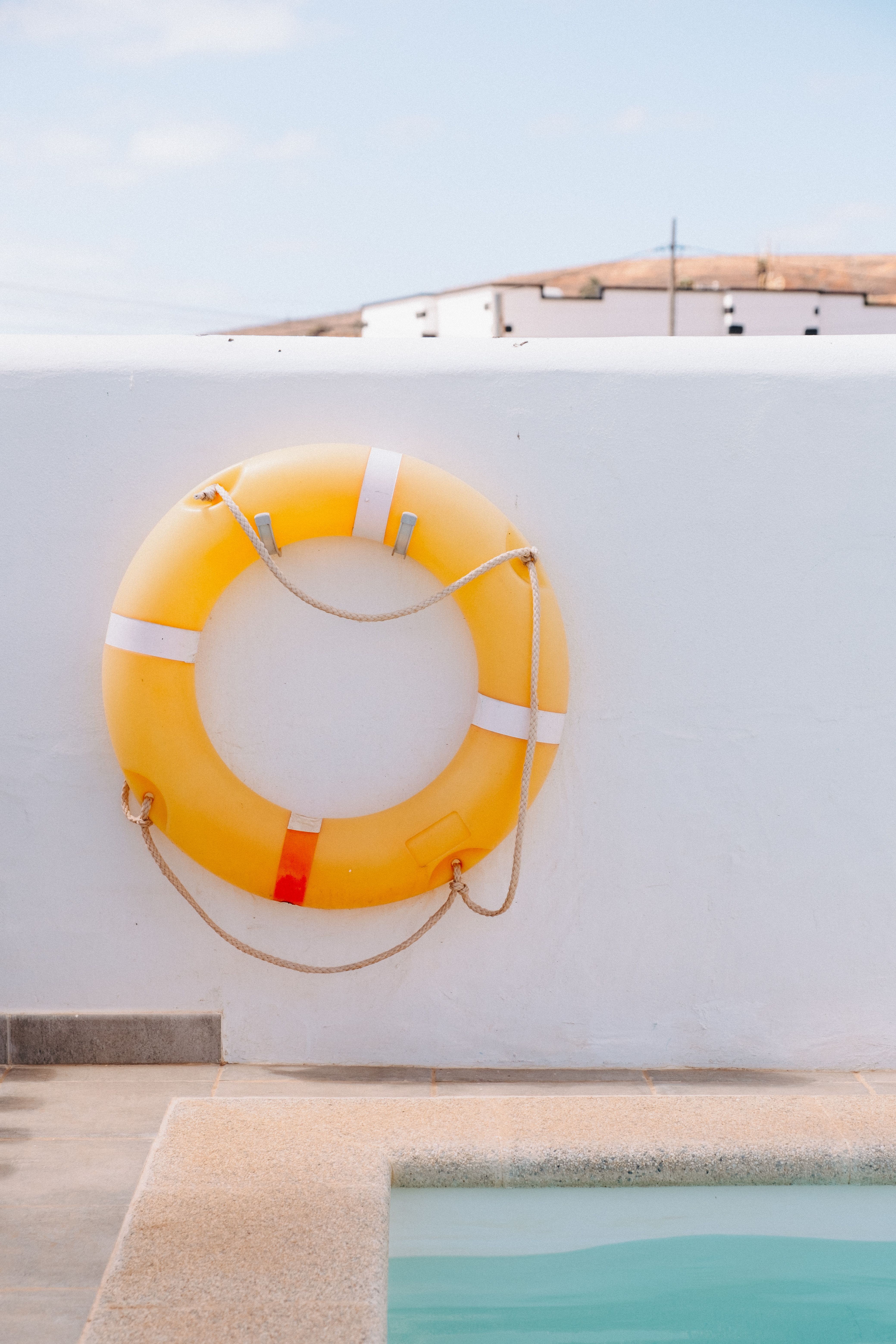 A yellow lifebuoy hangs on a white wall near a pool, exuding summer vibes.