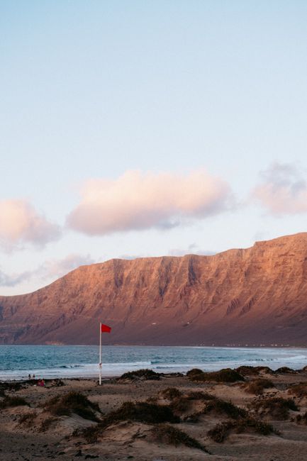 A beautiful beach at sunset with mountains in the background and a red flag waving in the breeze.