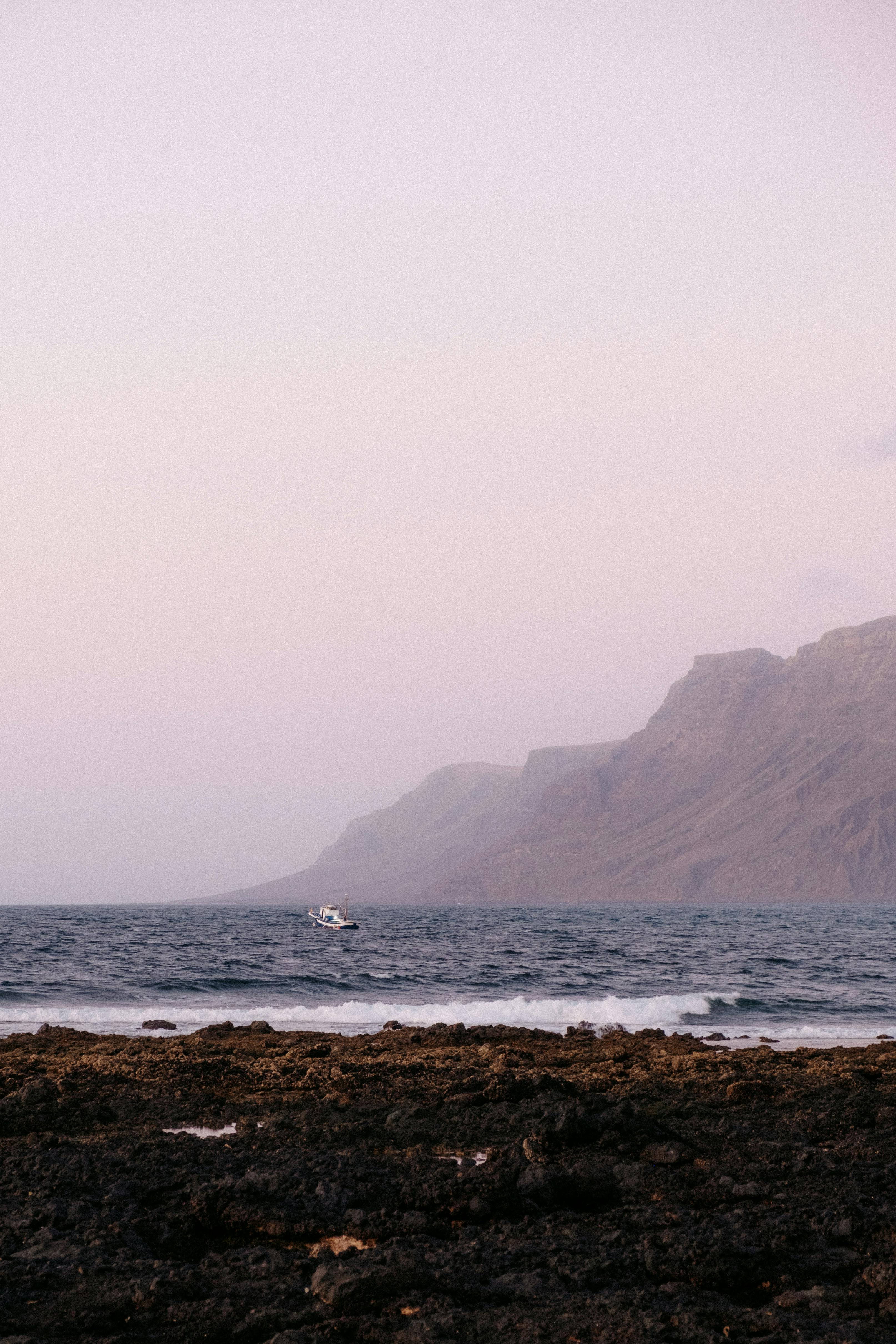 Serene view of a rocky seashore and ocean at twilight with a distant boat.