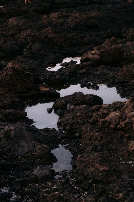 Captivating image of rugged volcanic rocks with water reflections at dusk, showcasing nature's raw beauty.
