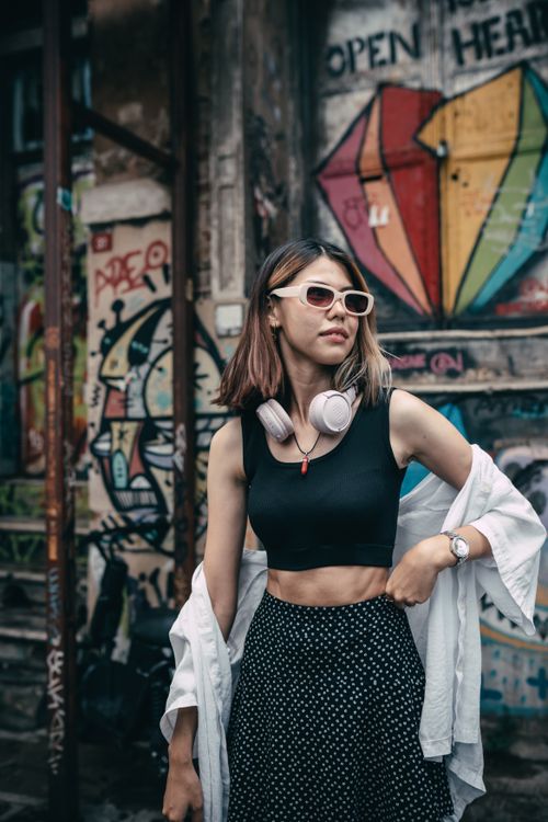 Free Stylish woman with sunglasses and headphones posing in front of colorful graffiti wall. Stock Photo
