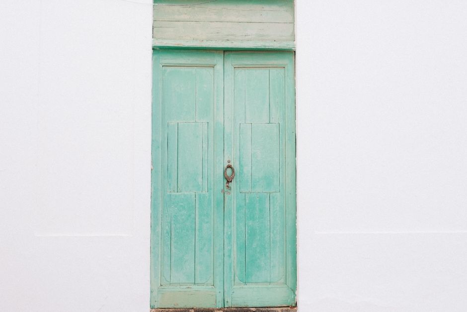 A rustic turquoise wooden door with a weathered look, set against a plain white wall.