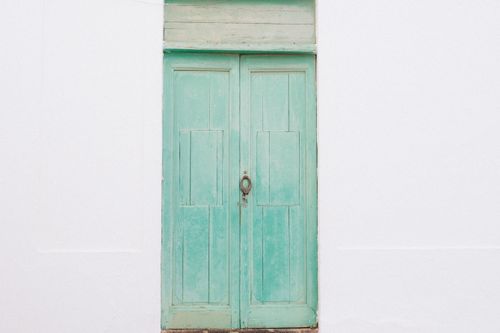 Free A rustic turquoise wooden door with a weathered look, set against a plain white wall. Stock Photo
