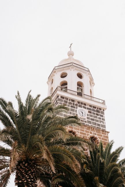 Beautiful stone church tower adorned with a cross and lush palm trees, capturing architectural elegance.