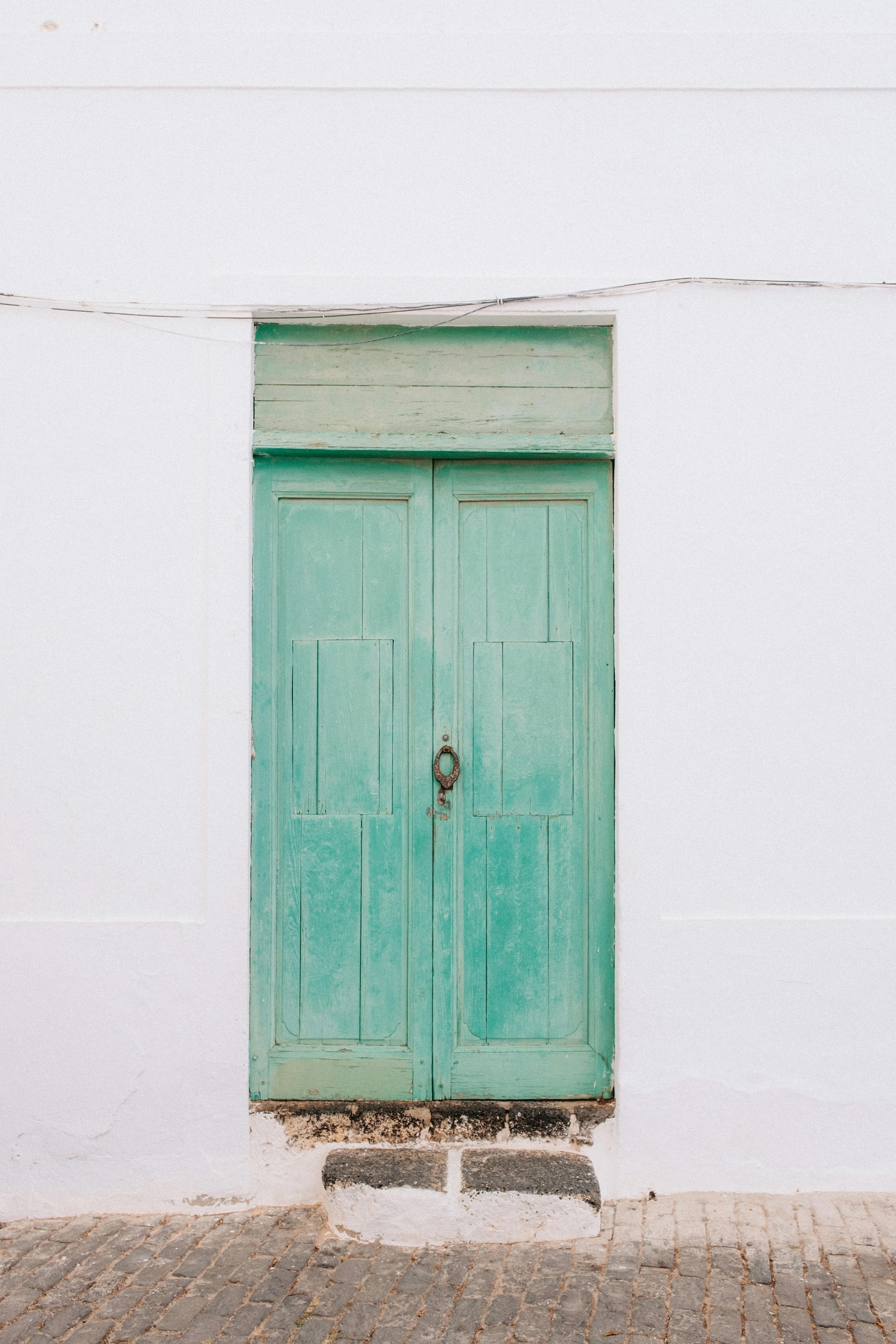 A rustic turquoise door on a white wall captures vintage charm and architectural beauty.