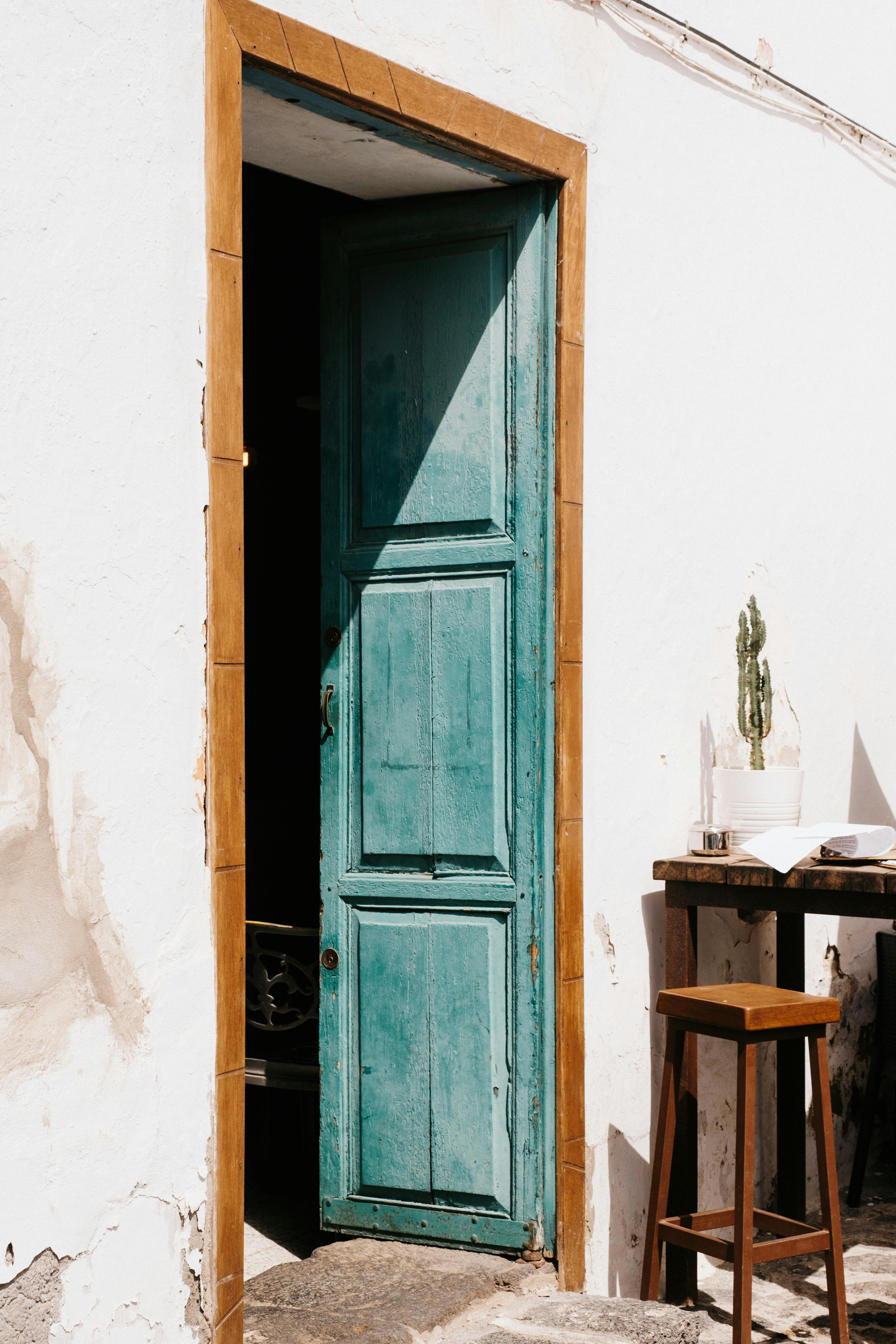 A charming rustic scene with a sunlit blue door, wooden table, and chair.