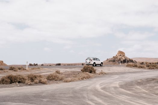 White SUV on an empty desert road with rocky formations and clear skies.
