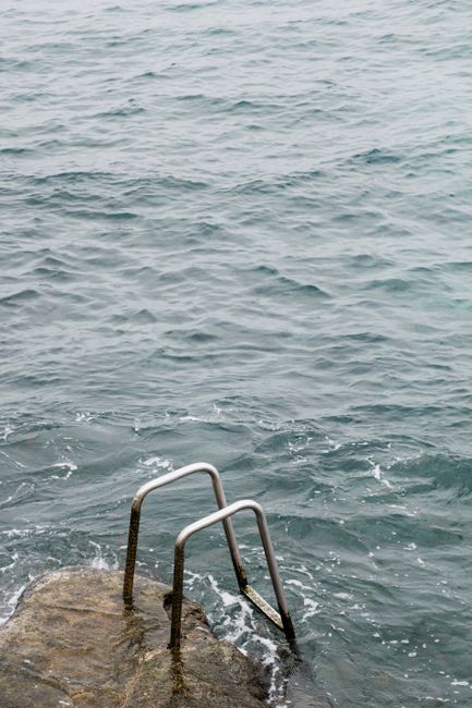 Metal ladder on rocky shore leading into ocean waves, perfect for summer or coastal themes.