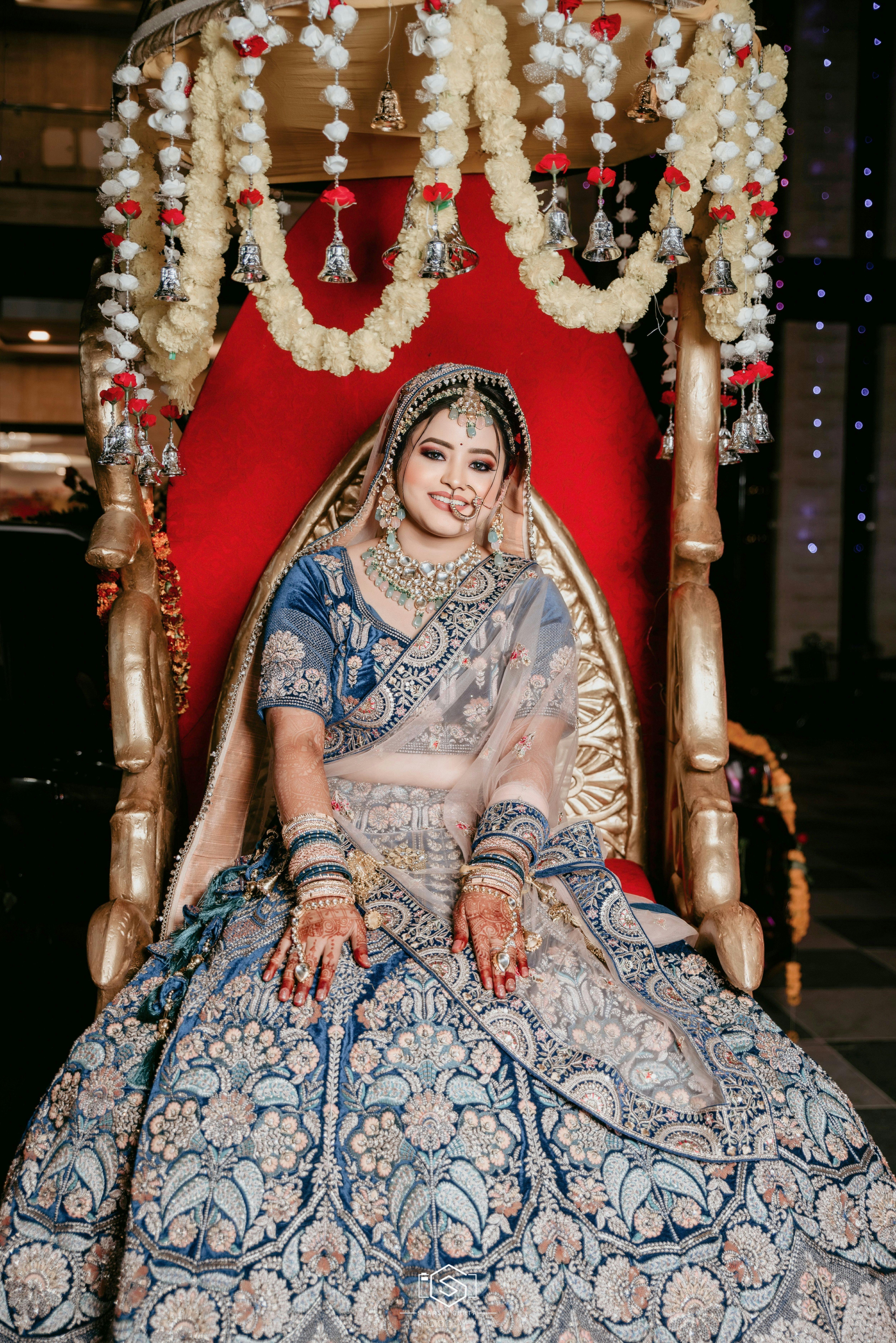 Beautiful Indian bride in ornate traditional dress seated in decorated setting at night.