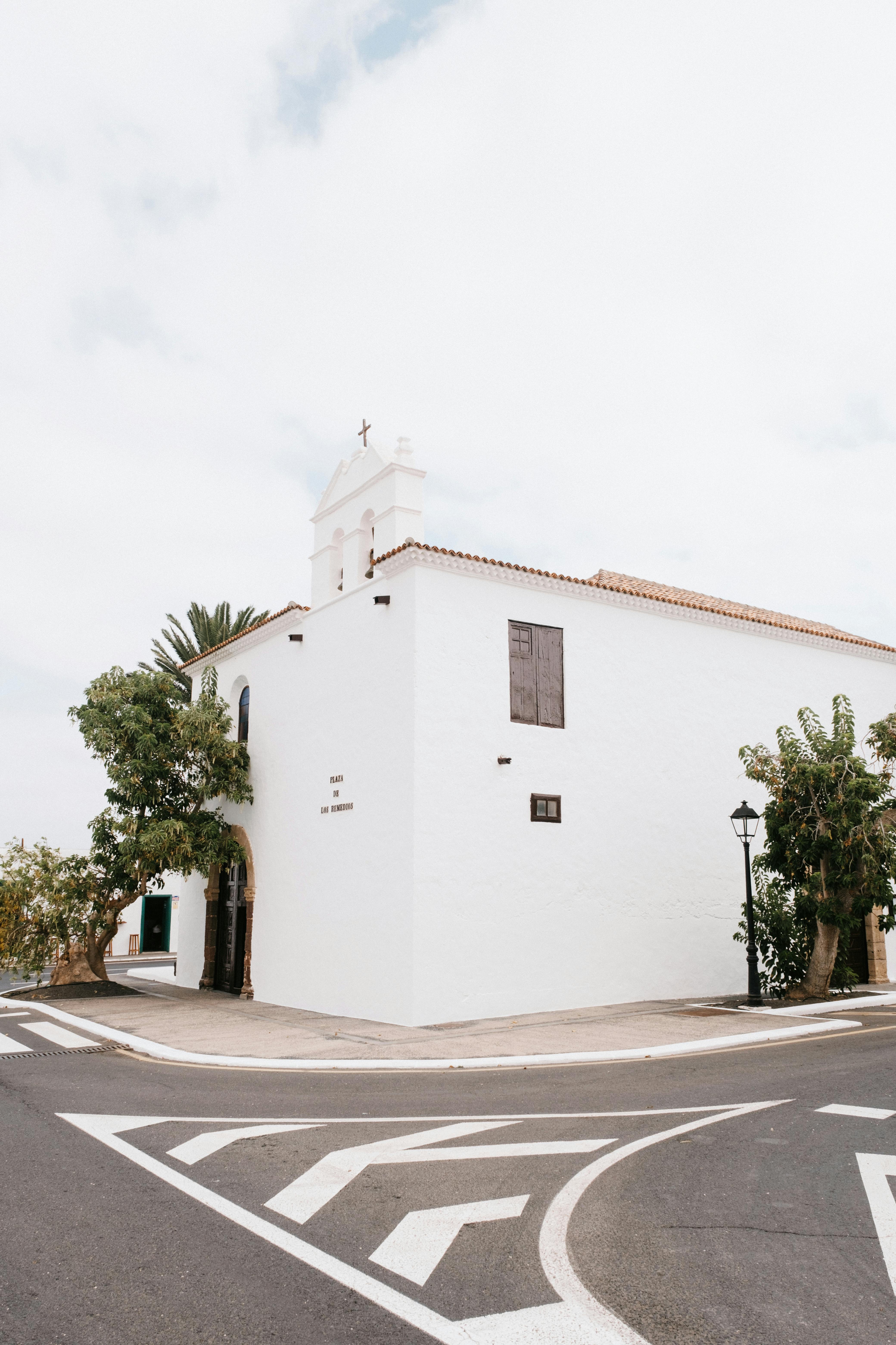 Free A serene white church with rustic charm on a clear summer day, captured at a street intersection. Stock Photo