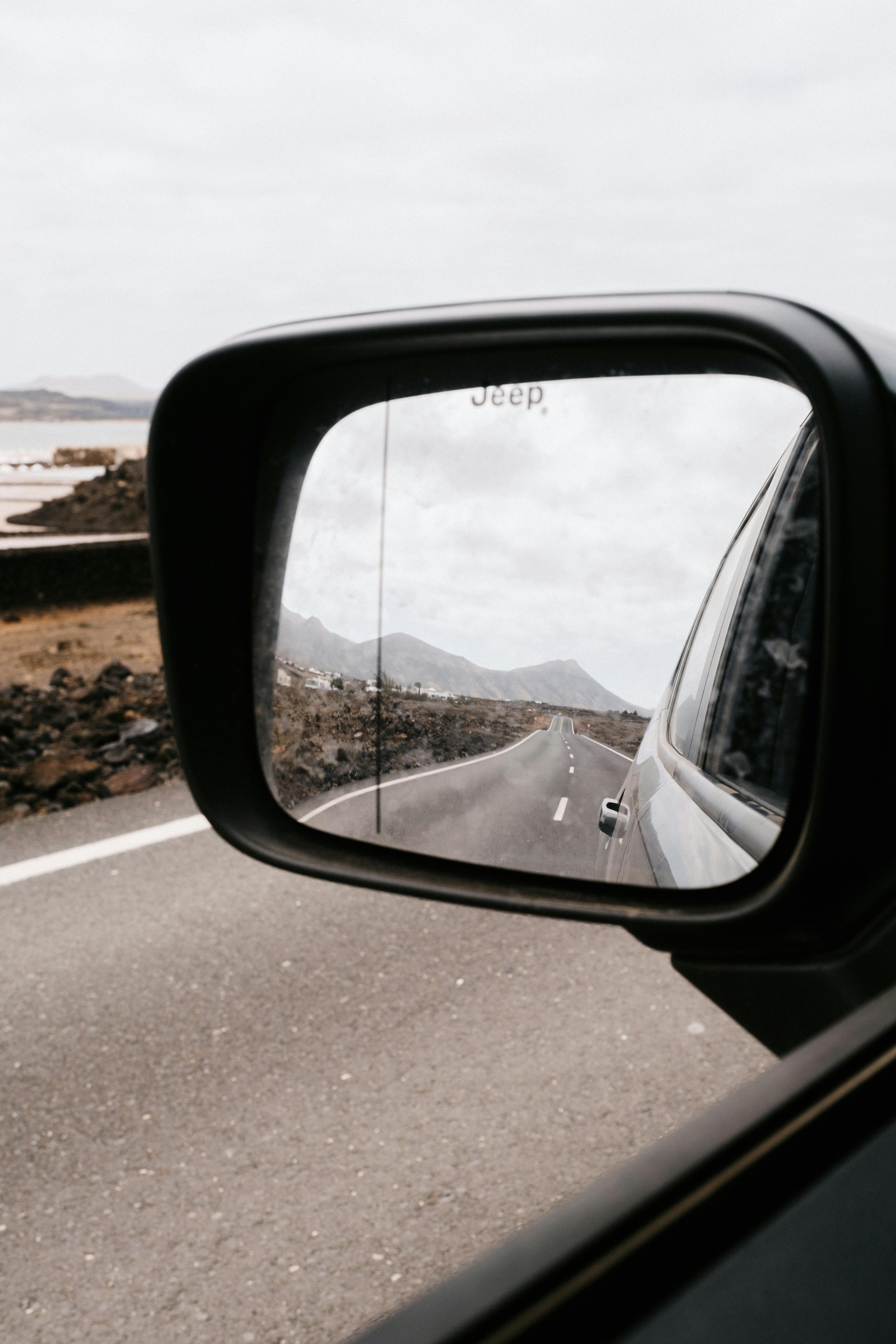 A scenic road view reflected in a car side mirror on an open highway.