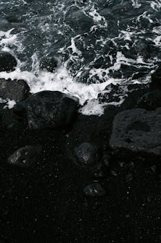 Moody seashore with dark rocks and crashing ocean waves.