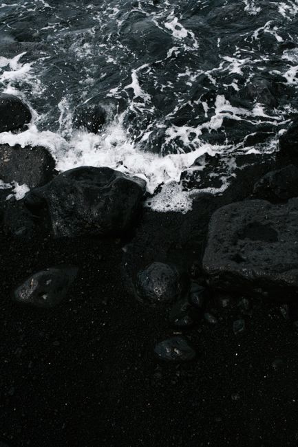 Moody seashore with dark rocks and crashing ocean waves.