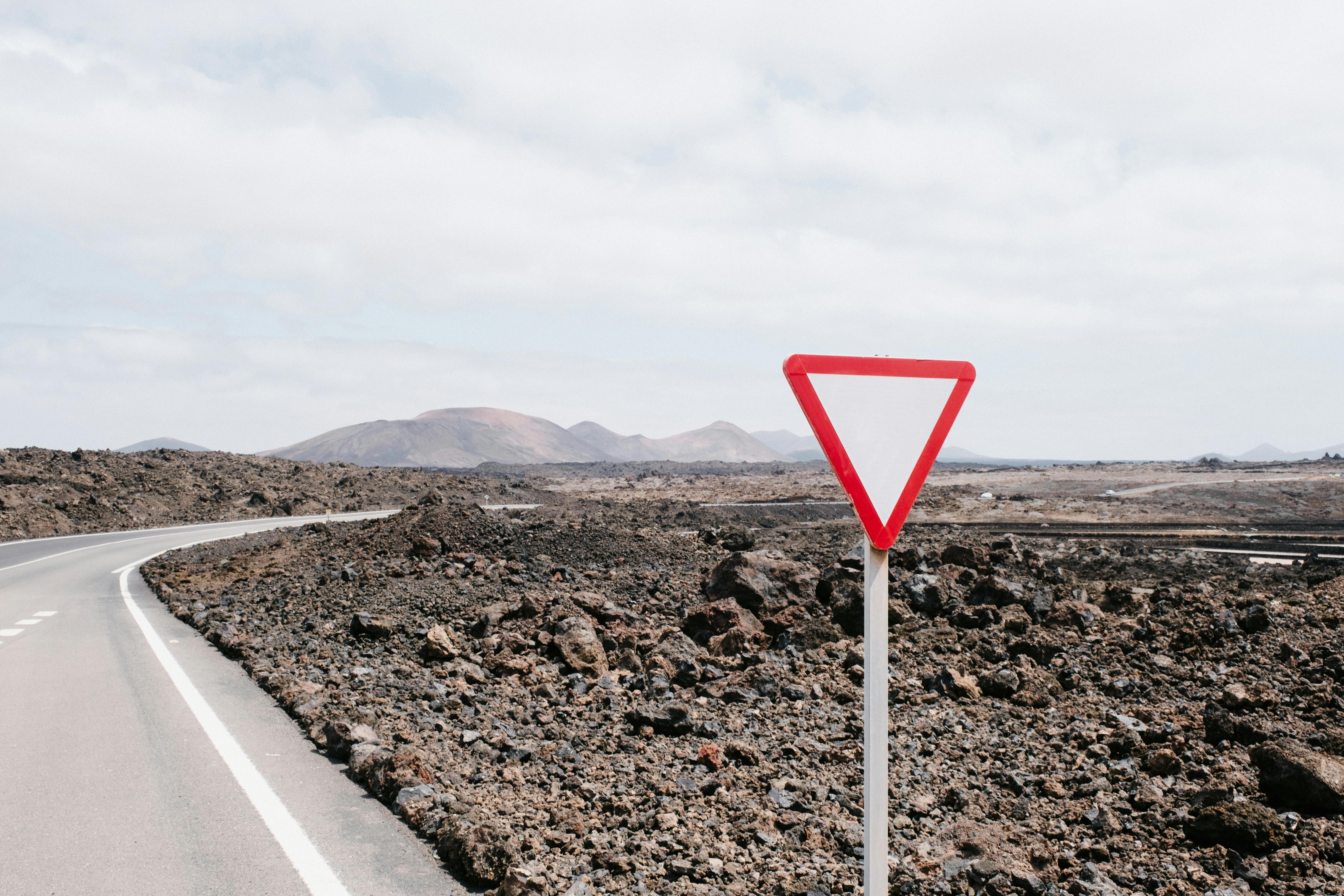 A deserted road in a rocky landscape with a yield sign under a cloudy sky.