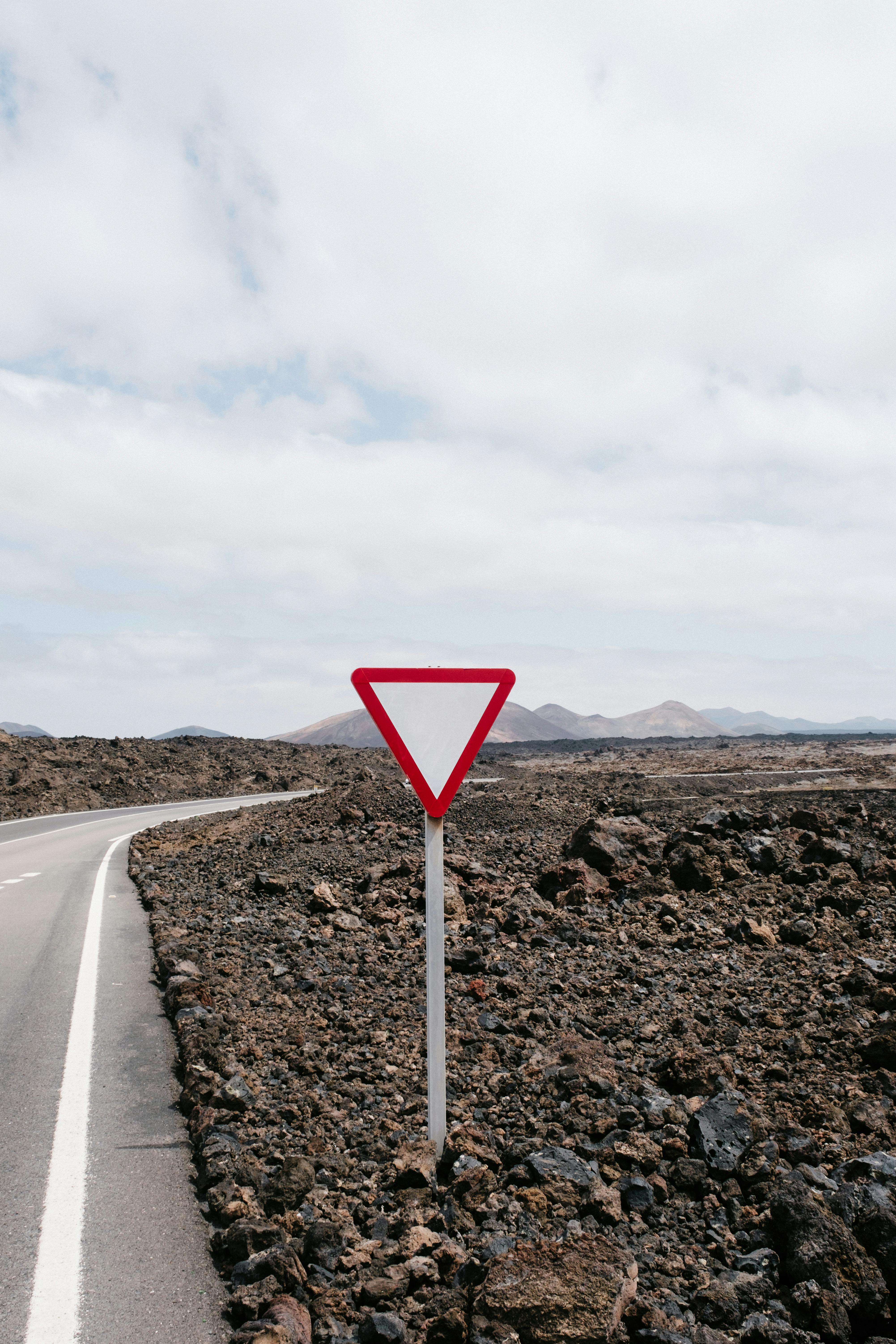 Yield sign on a deserted road through volcanic terrain under a cloudy sky.