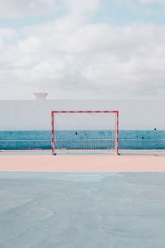 Empty soccer goal on a pastel-colored court under a cloudy sky.