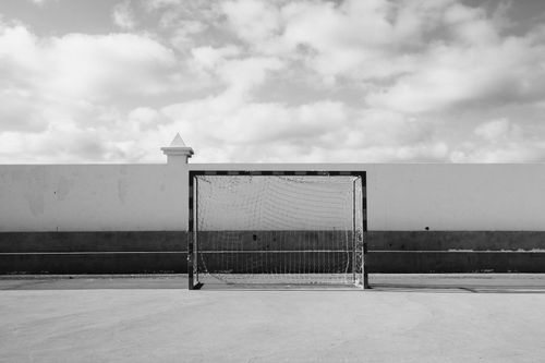 Free Empty soccer goal against a wall under a cloudy sky in black and white. Stock Photo