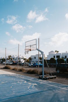 Basketball hoop on a street court in a sunny urban setting with cars and buildings nearby.