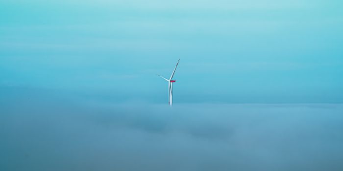 A lone wind turbine pierces through a dense fog, set against a clear blue sky, symbolizing sustainable energy.