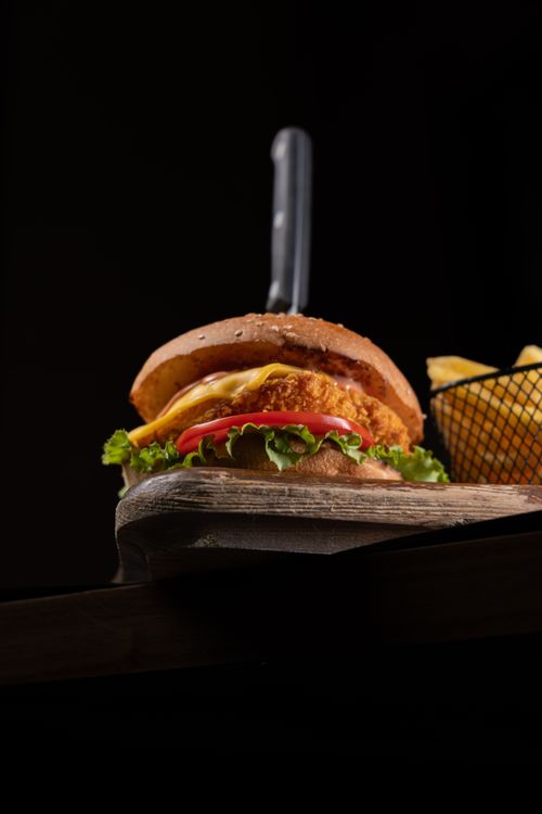 Free Close-up of a gourmet burger with cheese, lettuce, tomato, and fries. Perfect for fast food lovers. Stock Photo