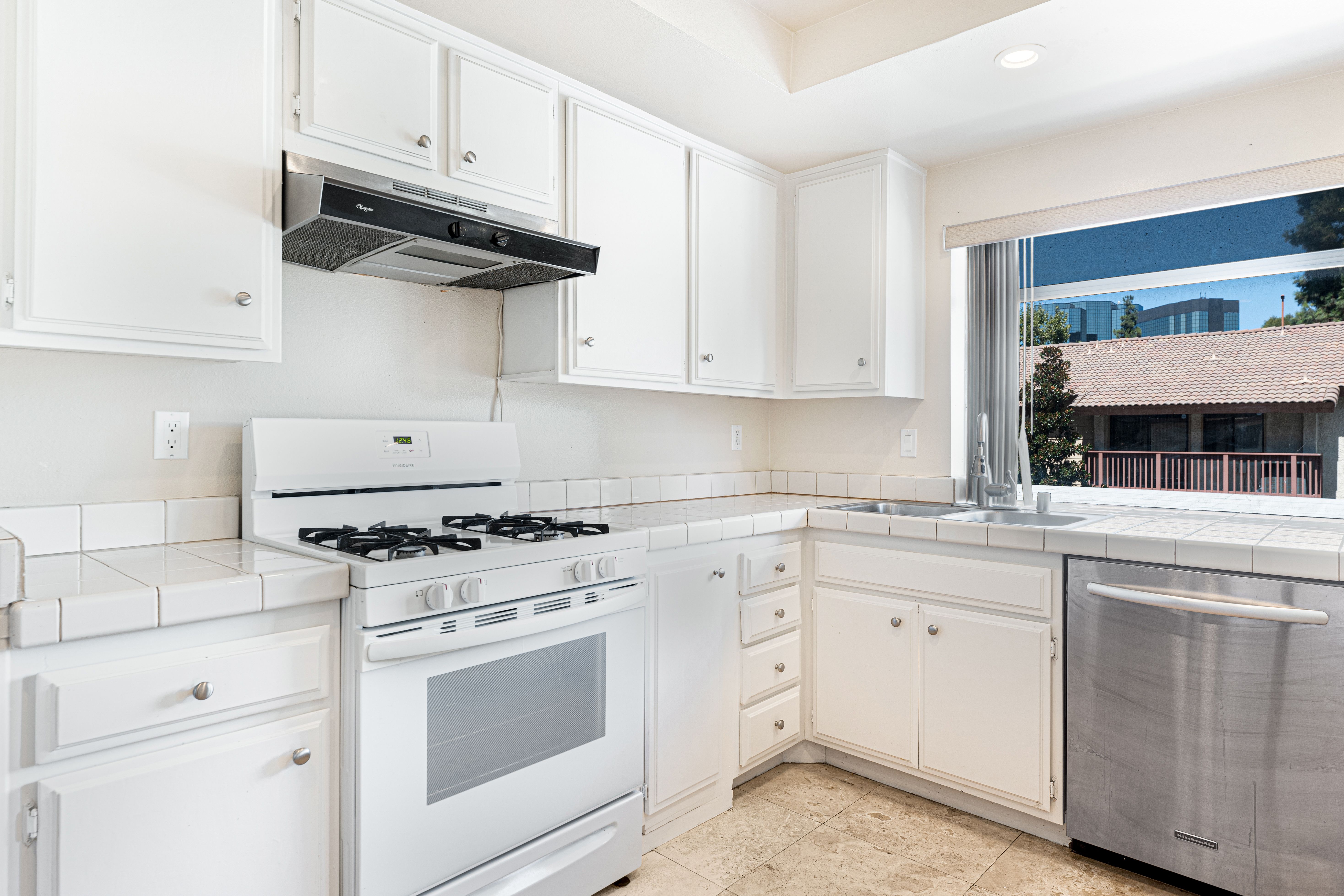 Spacious kitchen with white cabinets and stainless steel appliances featuring a sunlit view.