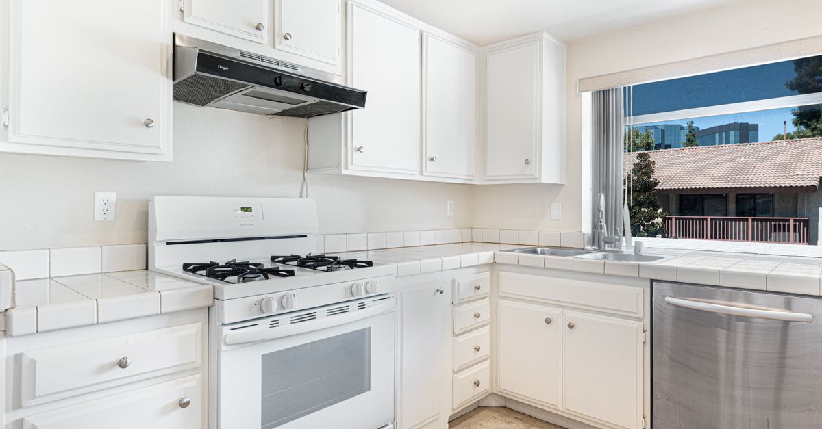 Spacious kitchen with white cabinets and stainless steel appliances featuring a sunlit view.