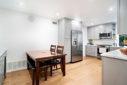Free Spacious minimalist kitchen featuring sleek cabinetry, stainless steel appliances, and a wooden dining table. Stock Photo