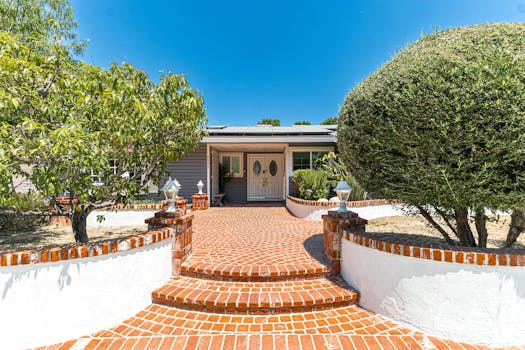 Charming entrance with red brick pathway leading to cozy house, surrounded by greenery.