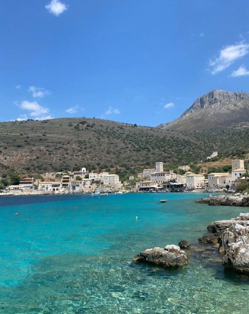 Free Picturesque coastal village in Greece with clear blue sea and mountainous backdrop. Stock Photo
