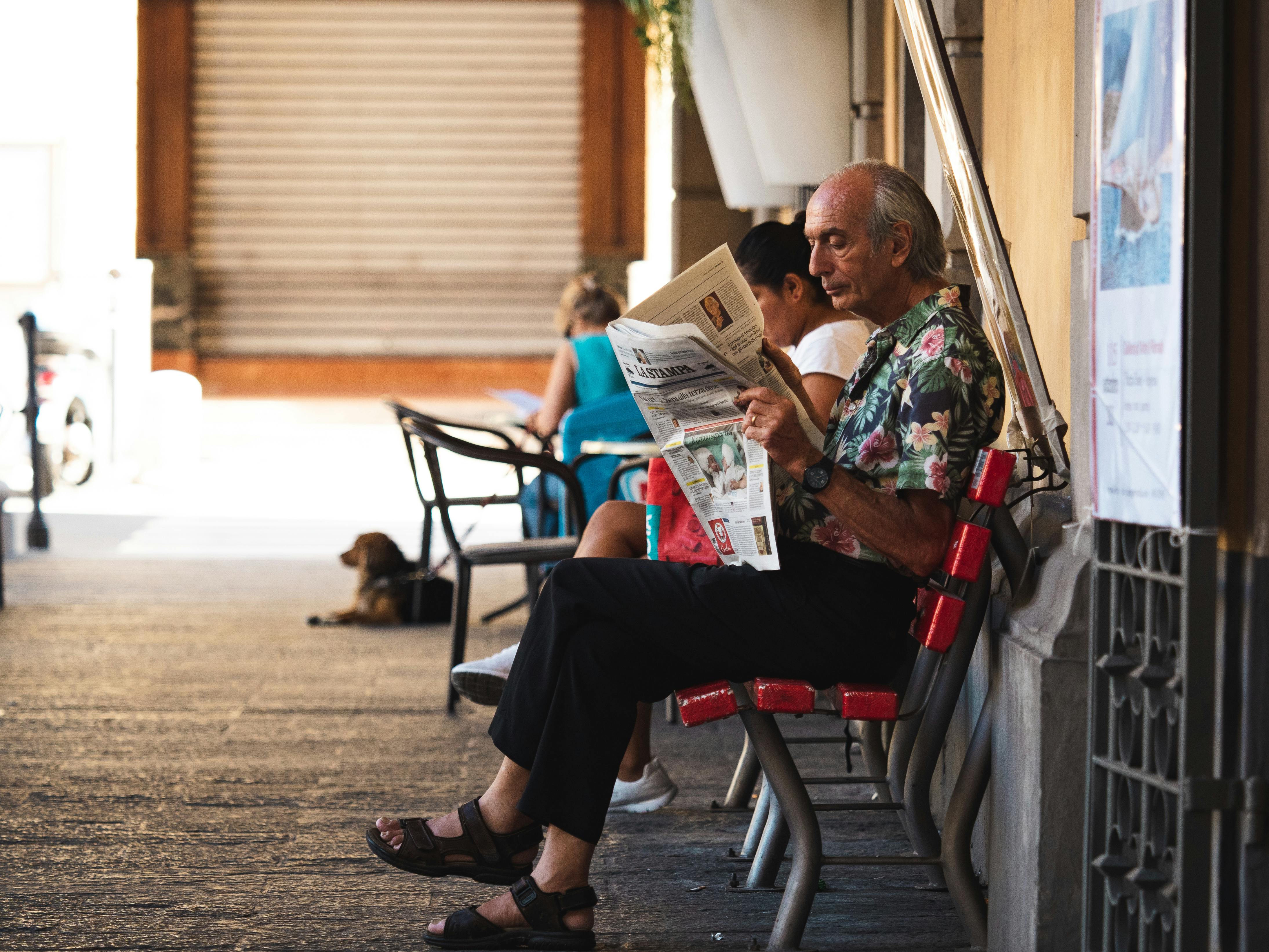 a man reading a newspaper on a bench