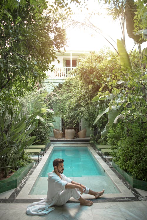 Man Sitting Near at Pool Side surrounded by Plants