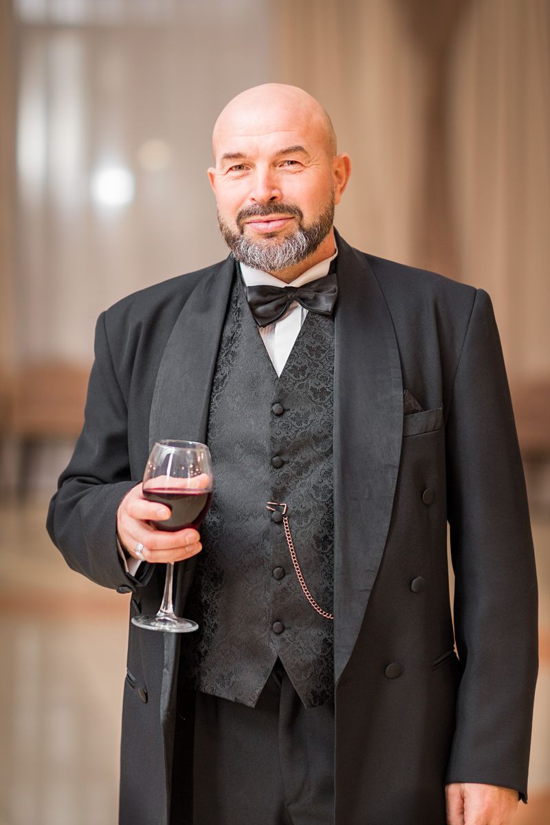 Portrait of a confident man in a tuxedo holding a glass of wine indoors.