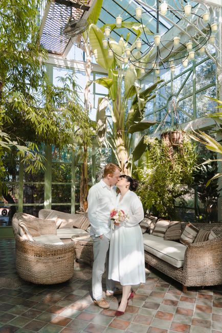 Loving couple kissing amidst lush greenery in a sunlit Moroccan greenhouse.