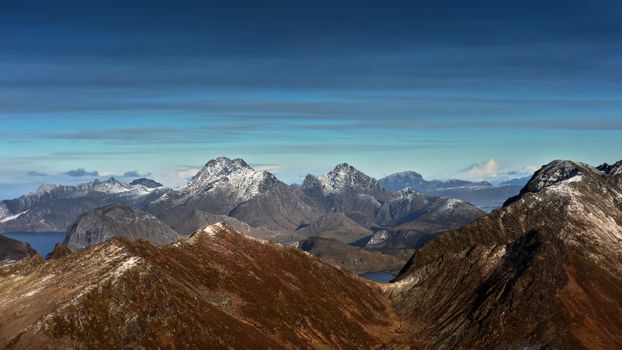 Breathtaking landscape of snow-capped mountains in Flakstad, Nordland, shot under clear skies.