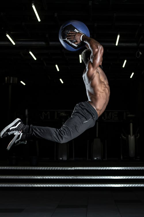 Free Man Jumping in Mid Air Holding Blue Ball Above His Head Stock Photo