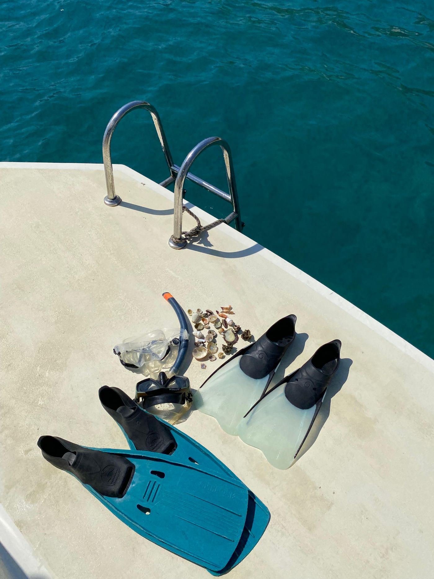 Snorkeling mask, snorkel, and fins organized on a boat beside clear water