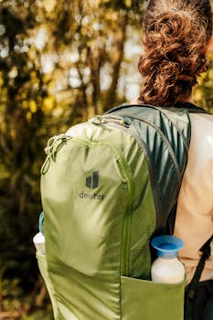 A woman with a green Deuter backpack hiking through a sunlit forest trail.